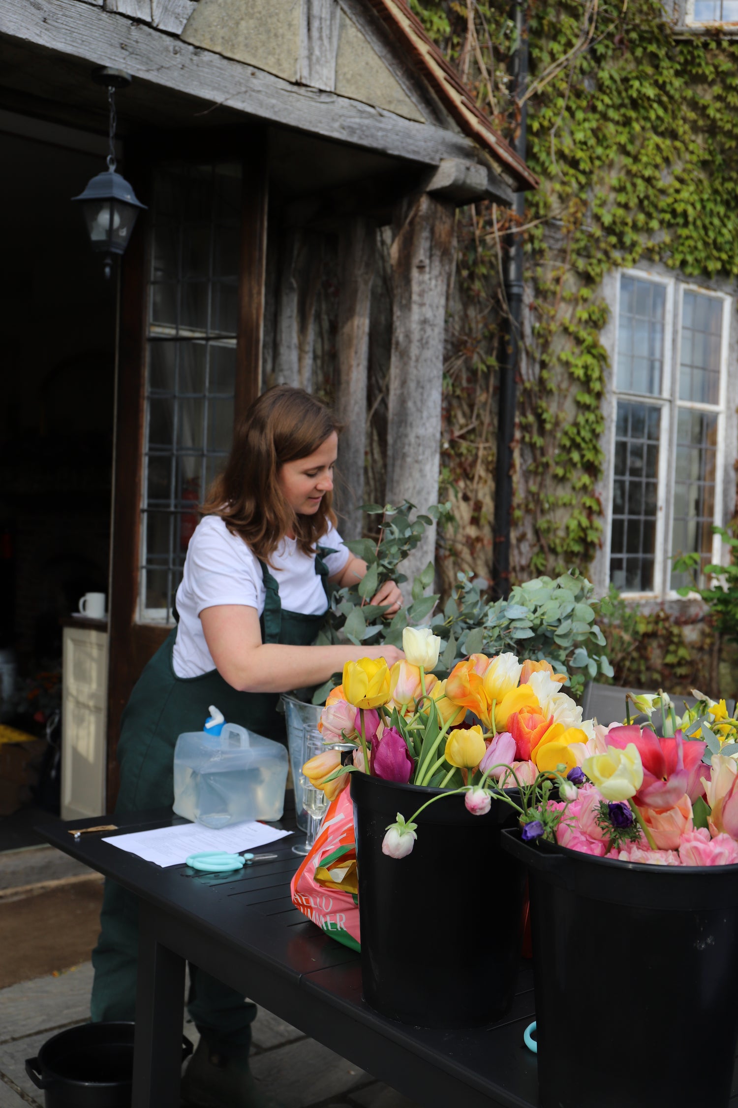 Woman arranging flowers with buckets of brightly coloured, sustainably grown flowers