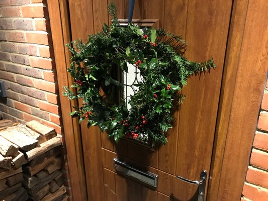 Festive wreath hung on front door; dark green with holly and ivy